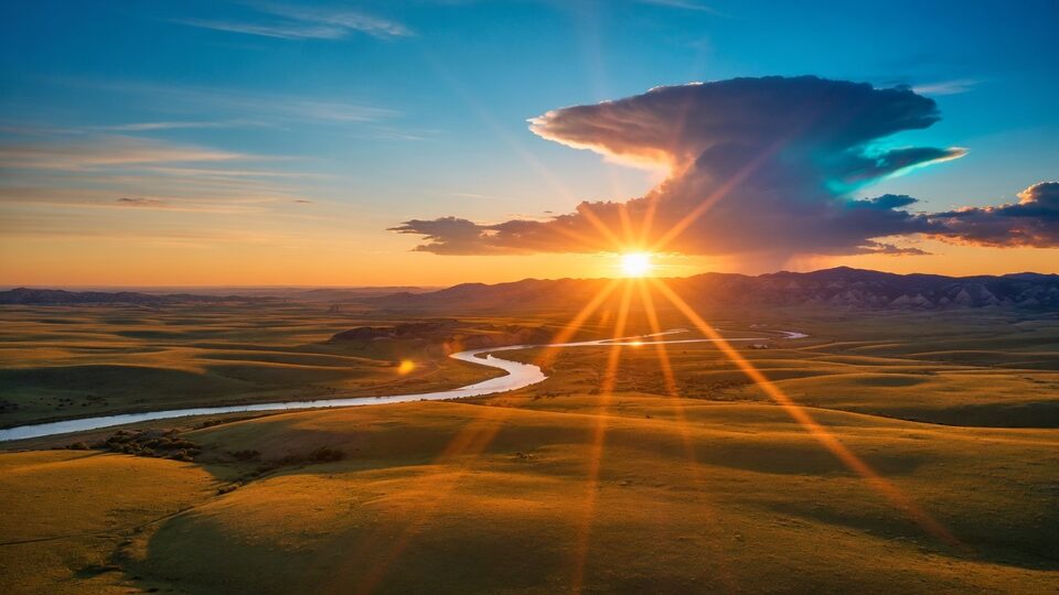 Aerial sunrise over a winding river, open hills, and a teal-lit cloud